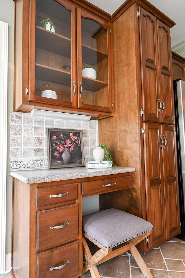 interior space with glass insert cabinets, brown cabinets, light countertops, and tasteful backsplash