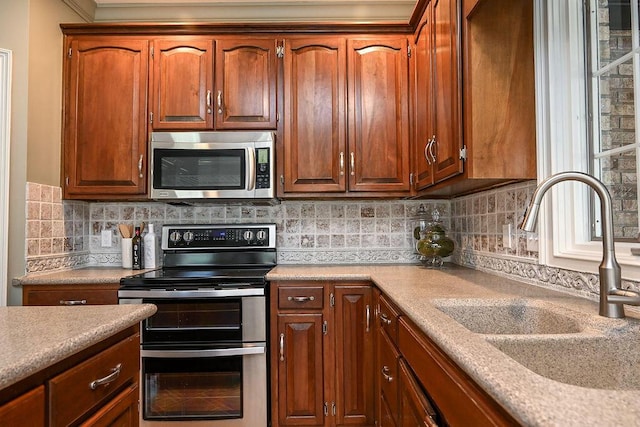 kitchen featuring tasteful backsplash, brown cabinetry, stainless steel appliances, light countertops, and a sink