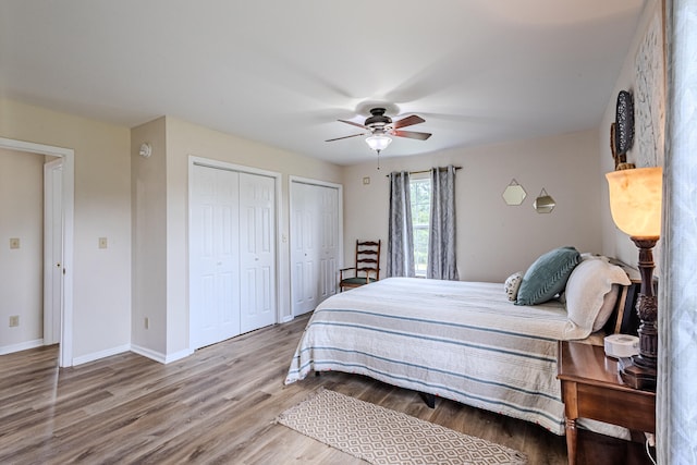 bedroom with ceiling fan, wood-type flooring, and two closets