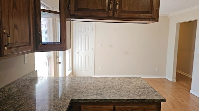 kitchen with dark brown cabinetry, dark stone counters, light hardwood / wood-style flooring, and crown molding