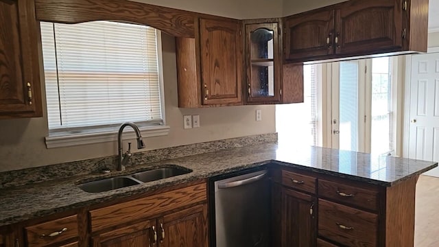 kitchen featuring kitchen peninsula, stainless steel dishwasher, dark stone counters, and sink