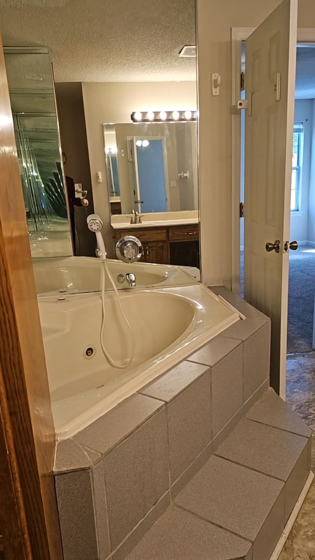 bathroom featuring vanity, a textured ceiling, and tiled tub