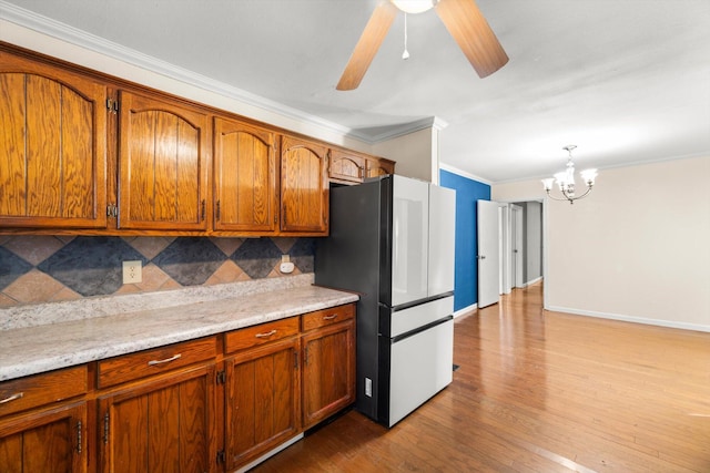 kitchen with refrigerator, tasteful backsplash, ceiling fan with notable chandelier, crown molding, and pendant lighting