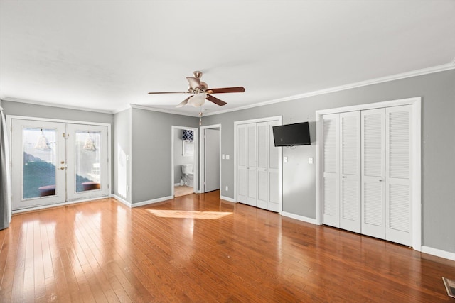 unfurnished bedroom with hardwood / wood-style flooring, ceiling fan, ornamental molding, and multiple closets