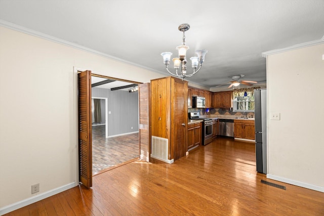 kitchen featuring appliances with stainless steel finishes, backsplash, crown molding, pendant lighting, and hardwood / wood-style flooring