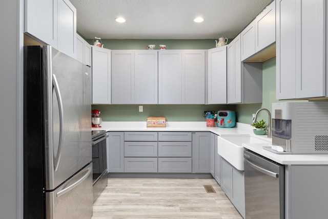 kitchen featuring sink, a textured ceiling, appliances with stainless steel finishes, gray cabinets, and light hardwood / wood-style floors