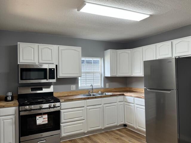 kitchen featuring white cabinetry, stainless steel appliances, sink, and butcher block countertops