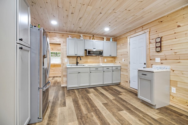 kitchen featuring wooden walls, wood ceiling, sink, and appliances with stainless steel finishes