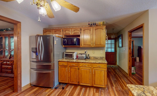 kitchen featuring ceiling fan, a textured ceiling, light hardwood / wood-style floors, light stone counters, and stainless steel fridge with ice dispenser