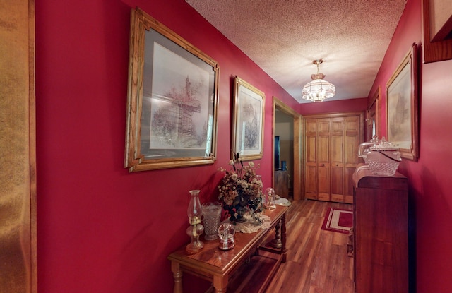 hall with a textured ceiling, hardwood / wood-style flooring, and a notable chandelier