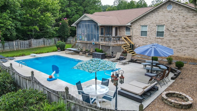 view of pool with a sunroom, a diving board, a deck, and a fire pit