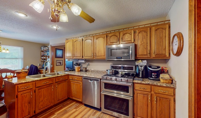 kitchen with kitchen peninsula, appliances with stainless steel finishes, light wood-type flooring, a textured ceiling, and sink