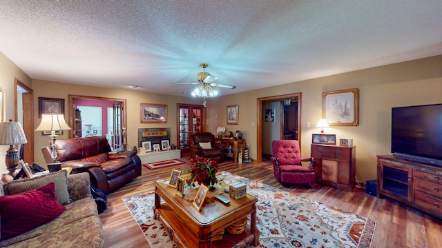 living room featuring a tiled fireplace, ceiling fan, a textured ceiling, and hardwood / wood-style flooring