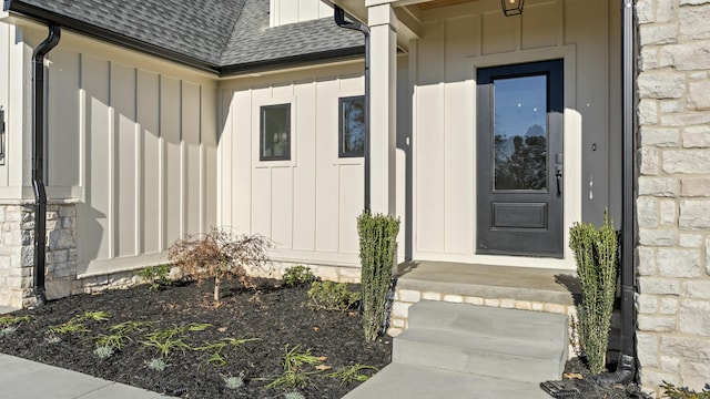 doorway to property with stone siding, board and batten siding, and roof with shingles