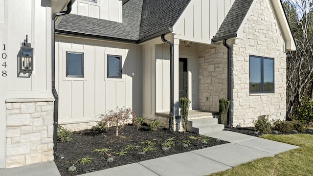 entrance to property with stone siding, board and batten siding, and a shingled roof