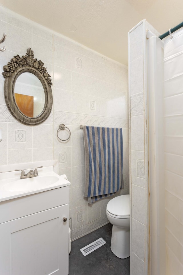 bathroom featuring tile patterned flooring, vanity, toilet, and tile walls