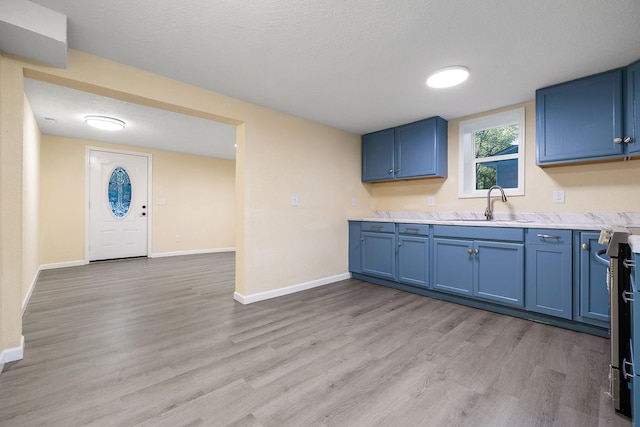 kitchen featuring sink, blue cabinets, a textured ceiling, and light wood-type flooring