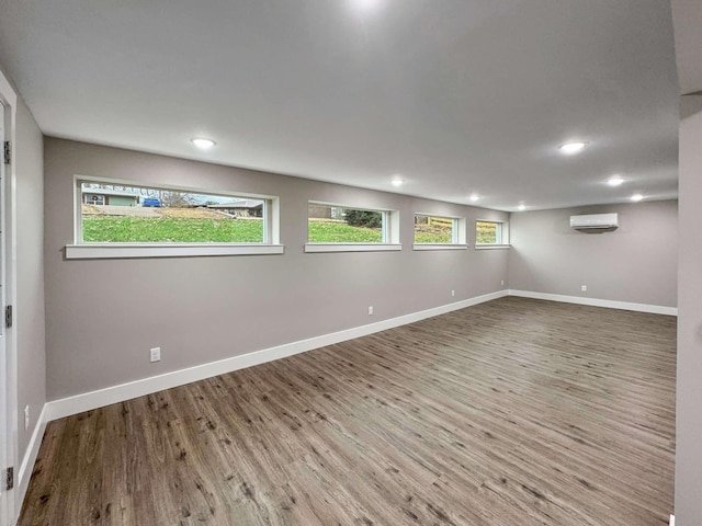 basement with hardwood / wood-style floors, an AC wall unit, and a healthy amount of sunlight