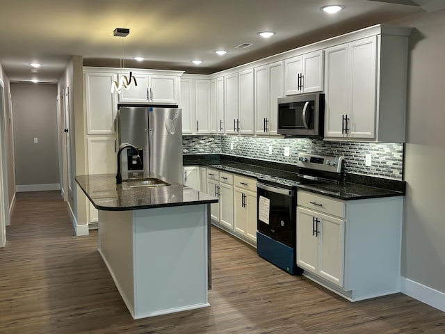 kitchen with a center island with sink, dark stone countertops, pendant lighting, stainless steel appliances, and white cabinets