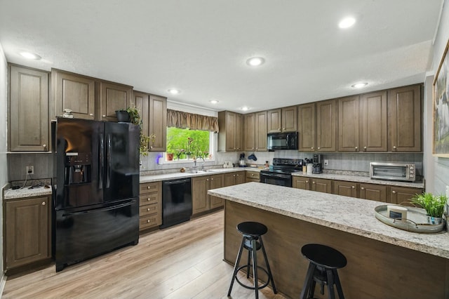 kitchen with light wood-type flooring, a toaster, a breakfast bar area, decorative backsplash, and black appliances