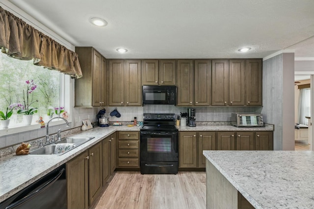 kitchen featuring light countertops, light wood-style floors, a sink, and black appliances