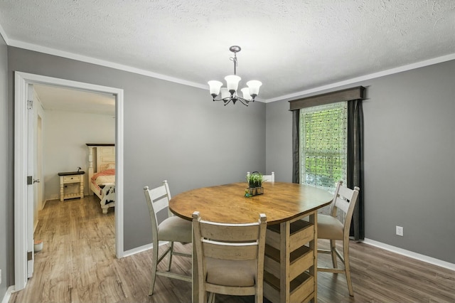 dining space featuring light wood-style floors, crown molding, an inviting chandelier, a textured ceiling, and baseboards