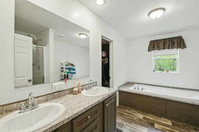 bathroom featuring a stall shower, a garden tub, wood finished floors, and a sink