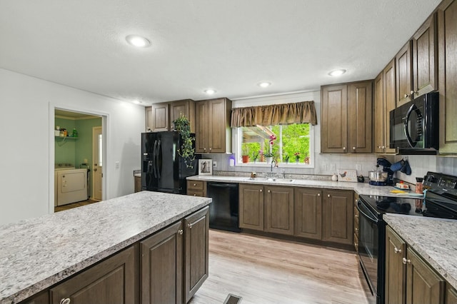 kitchen with tasteful backsplash, a sink, light wood-type flooring, black appliances, and washer and clothes dryer