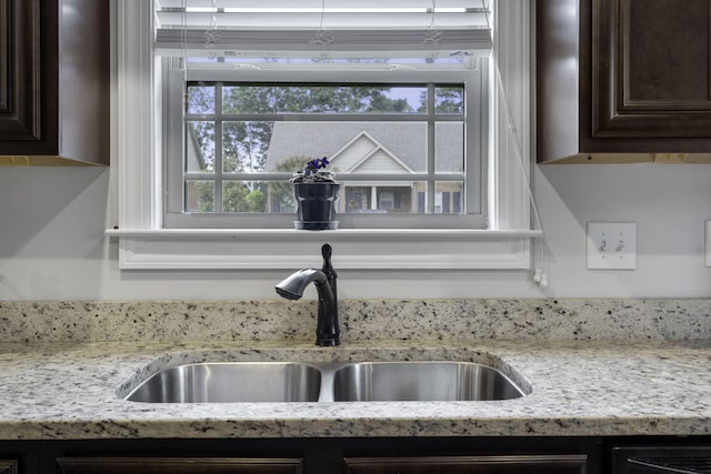 room details featuring light stone countertops, dark brown cabinets, and sink