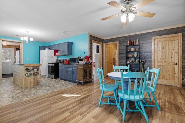 dining room with ceiling fan with notable chandelier, light hardwood / wood-style floors, and wood walls