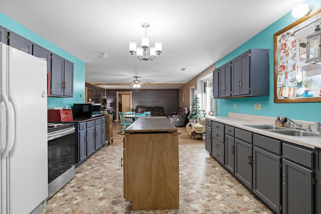 kitchen featuring pendant lighting, ceiling fan with notable chandelier, sink, wooden walls, and appliances with stainless steel finishes