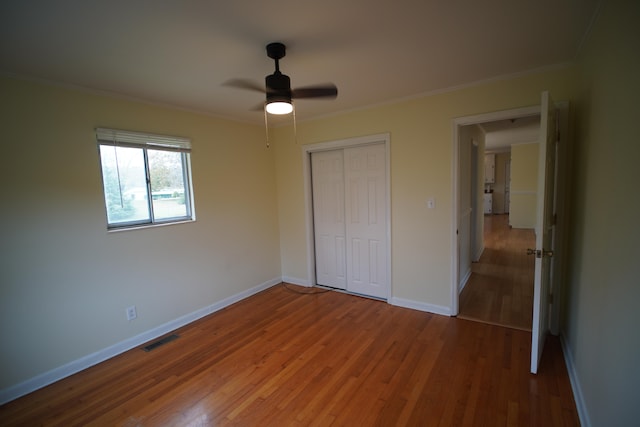 unfurnished bedroom featuring hardwood / wood-style floors, ceiling fan, ornamental molding, and a closet