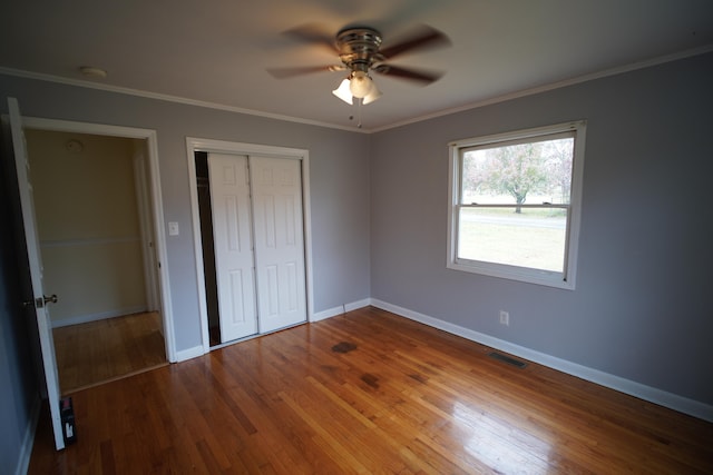 unfurnished bedroom featuring a closet, hardwood / wood-style flooring, ceiling fan, and crown molding