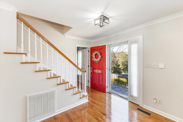 foyer entrance with ornamental molding, wood finished floors, visible vents, and baseboards