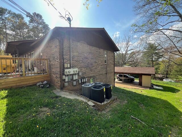 view of property exterior featuring brick siding, a deck, central AC, and a yard