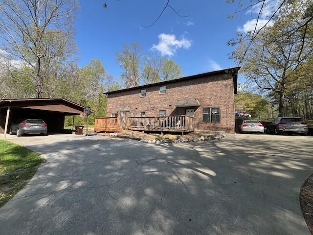 view of side of property featuring brick siding, a deck, aphalt driveway, and a carport