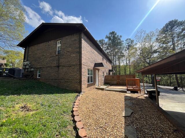 view of home's exterior with a lawn, a deck, fence, and brick siding