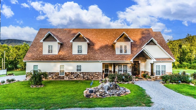 view of front of house with stone siding, roof with shingles, and a front lawn