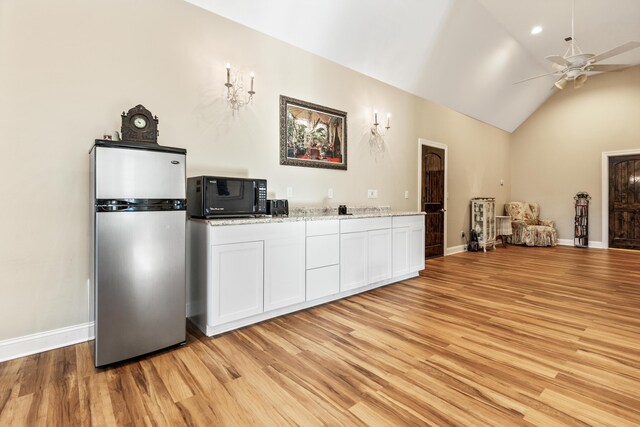 kitchen with black microwave, white cabinetry, light wood-style floors, vaulted ceiling, and freestanding refrigerator