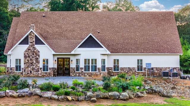 back of property featuring stone siding, cooling unit, french doors, and roof with shingles