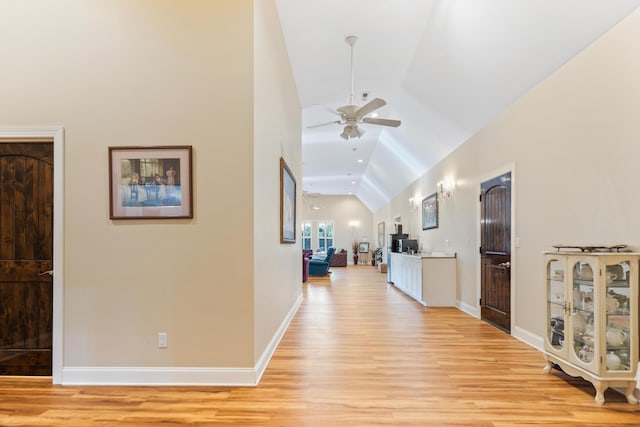 hallway featuring light wood-style floors, vaulted ceiling, and baseboards