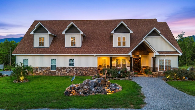 view of front facade featuring a front yard, stone siding, and roof with shingles