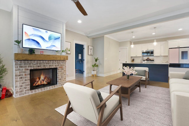 living room featuring ceiling fan, crown molding, light hardwood / wood-style floors, and a brick fireplace