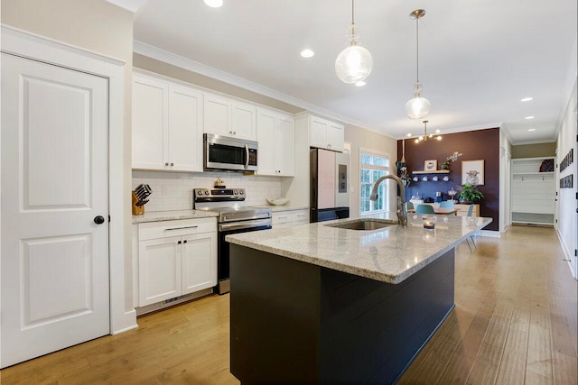 kitchen with a kitchen island with sink, pendant lighting, white cabinets, and stainless steel appliances