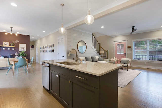 kitchen featuring dishwasher, sink, light stone countertops, an island with sink, and decorative light fixtures