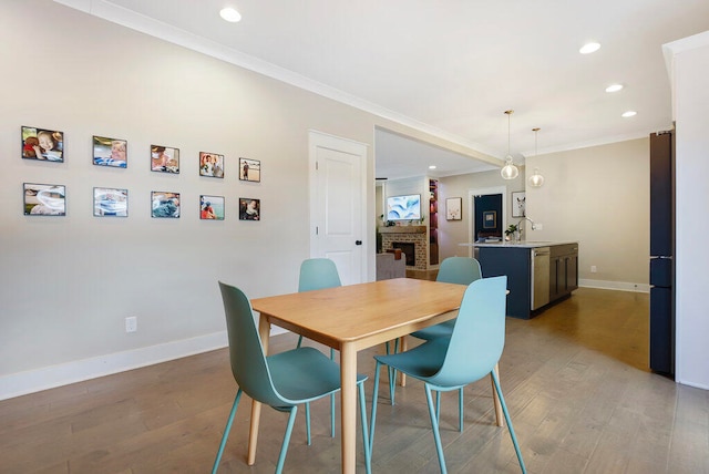 dining room featuring sink, crown molding, wood-type flooring, and a fireplace