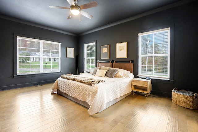 bedroom featuring light hardwood / wood-style flooring, multiple windows, ornamental molding, and ceiling fan