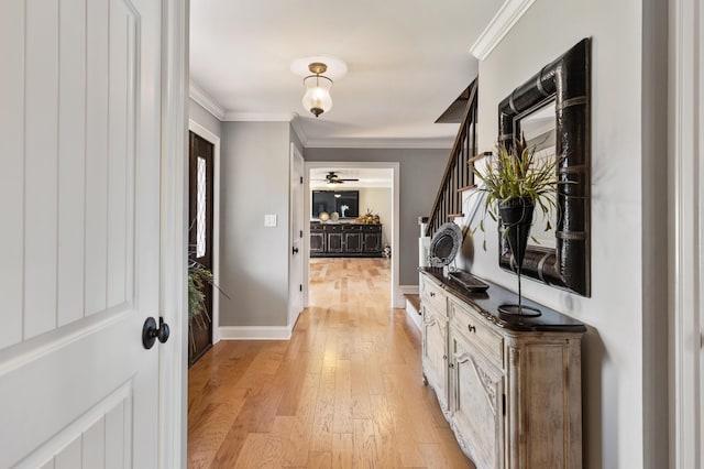 hallway with light wood-style flooring, baseboards, ornamental molding, and stairway