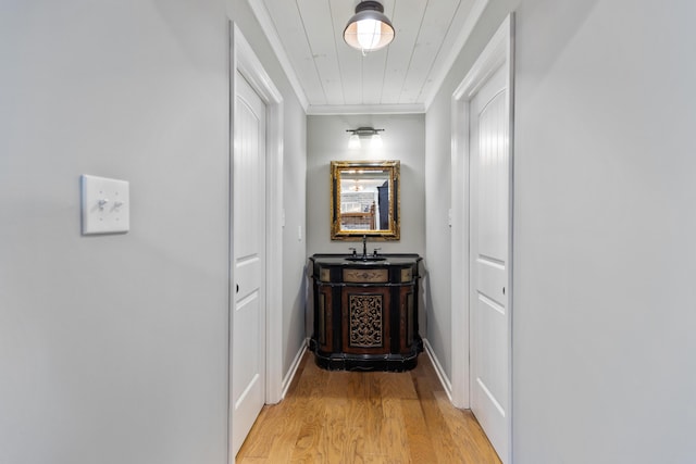 hallway featuring a sink, light wood-type flooring, baseboards, and ornamental molding