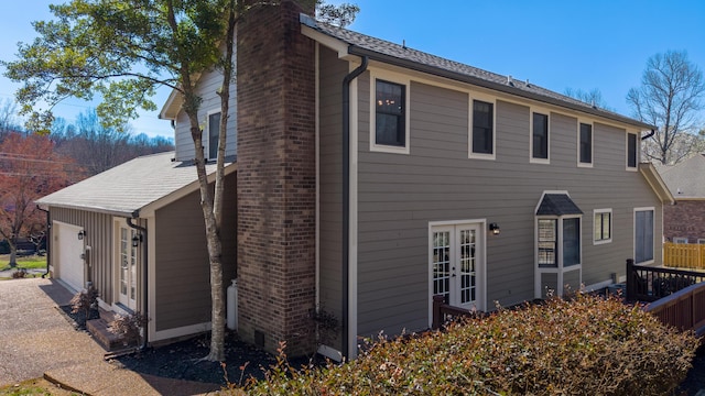 view of property exterior featuring brick siding, french doors, a chimney, and driveway